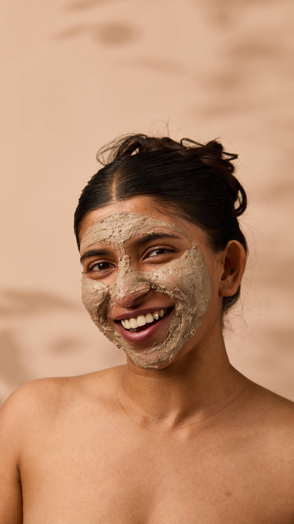 An image of the model's face on a warm, beige background. They have a smudge of the thick, creamy Nutkins face mask over their entire face as they smile.