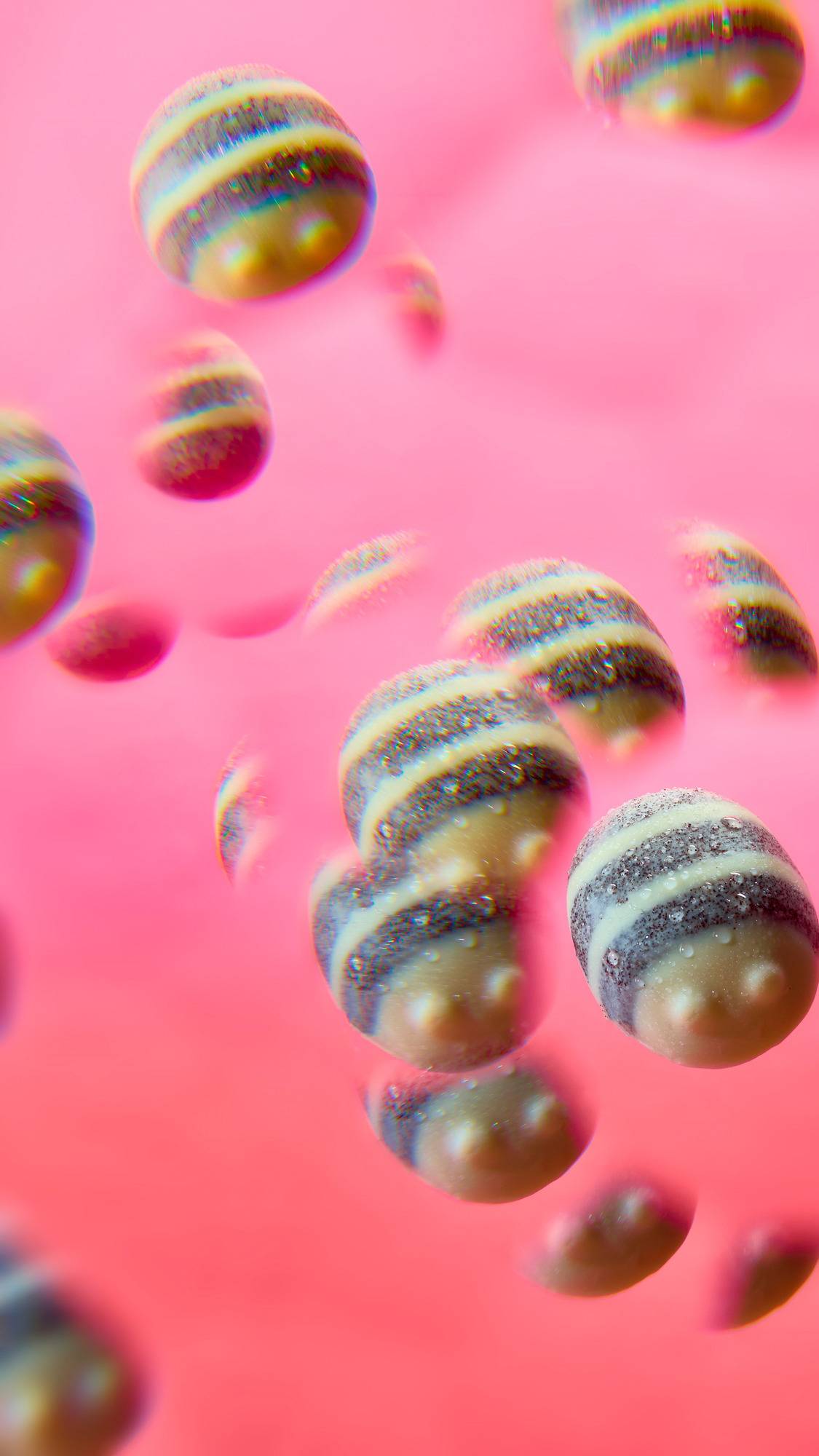 A kaleidoscopic, distorted view of a striped, bee-shaped massage bar. Multiple repeated, overlapping images of the cream-and-dark-grey product float dreamily against a bright pink background, creating a whimsical, surreal pattern.